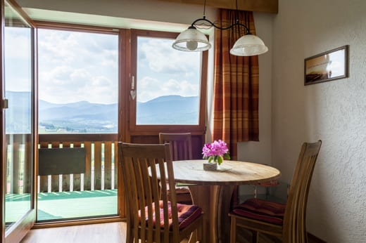 Runder Holztisch mit vier Stühlen am Fenster, daneben die offene Balkontür mit Blick auf die Berge